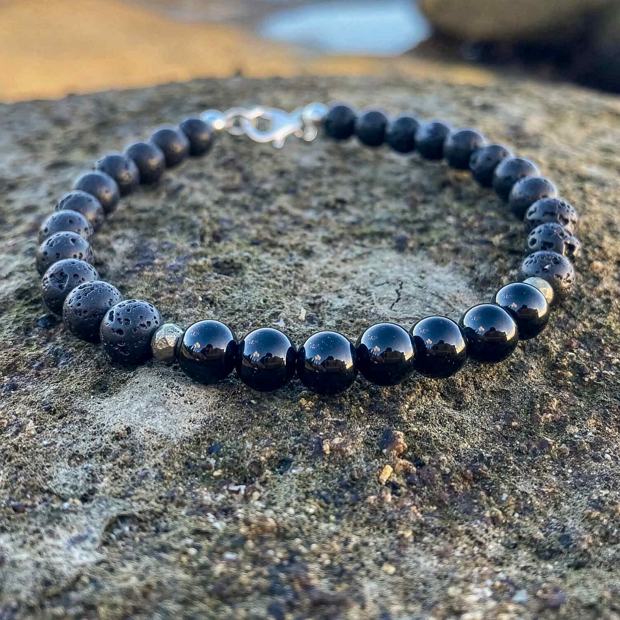 Black tourmaline and lava stone men’s bracelet photographed on a coastal rock