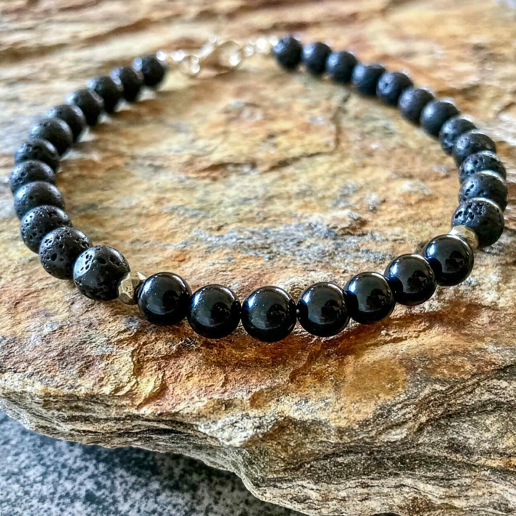 Black tourmaline and lava stone men’s bracelet resting on natural stone surface