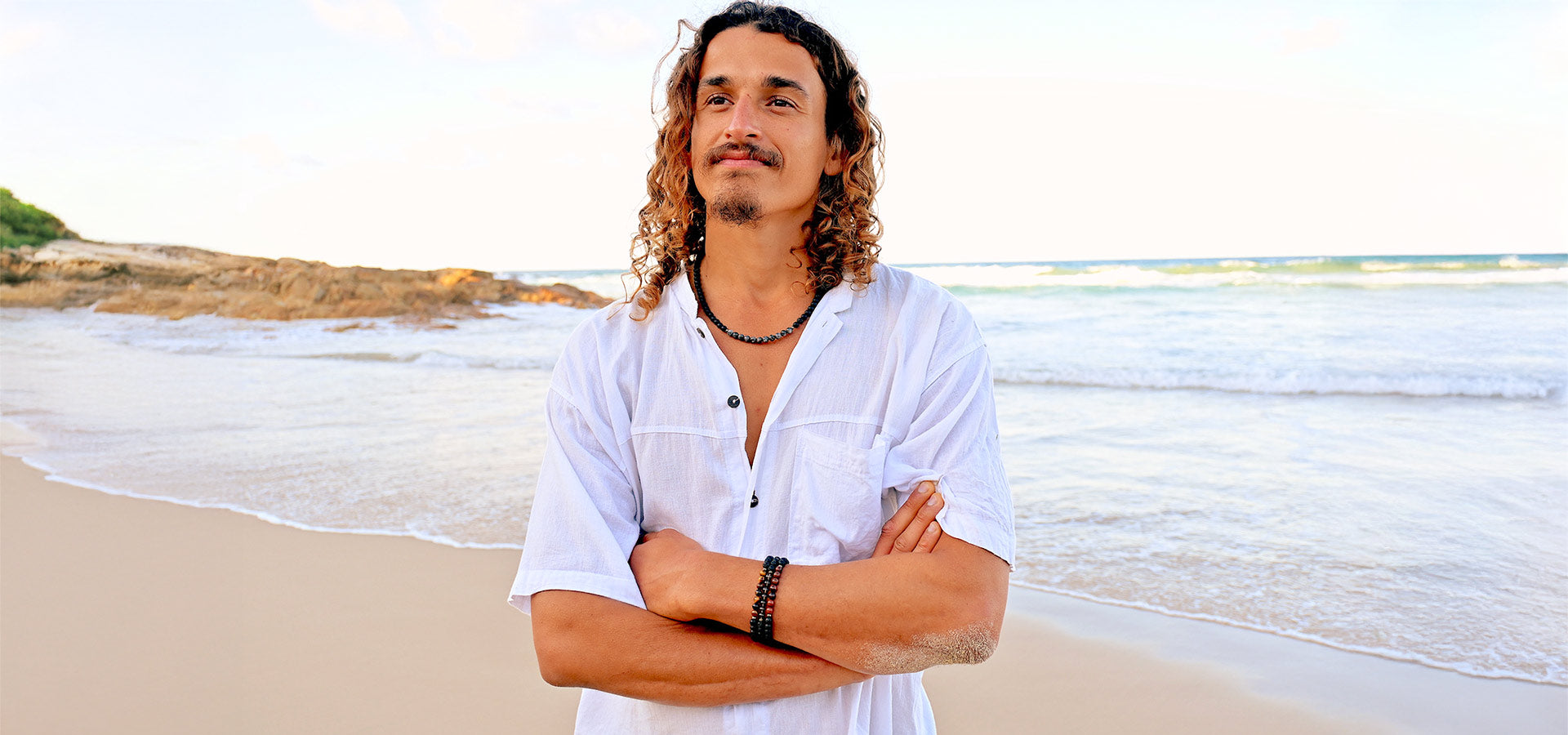 Mana for Men: Man on beach wearing three crystal bracelets and a necklace. Shop by intention.