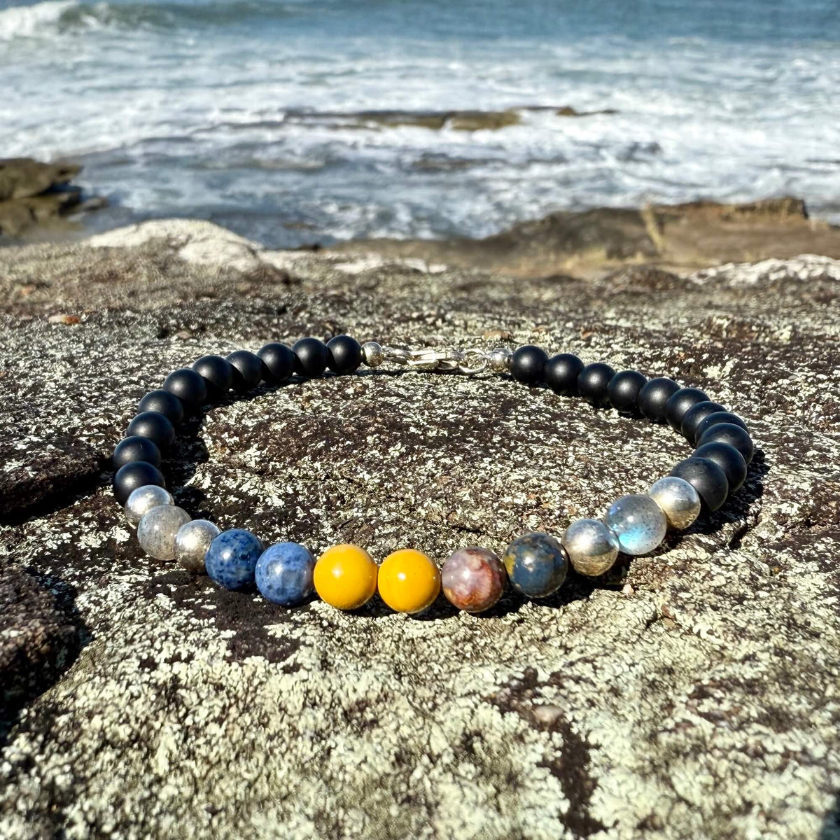 Phoenix Rising bracelet's five-stone centre on a rock by the ocean