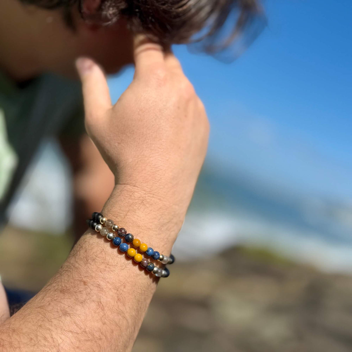 Phoenix Rising bracelet on a man's wrist as he touches his hair, sky behind
