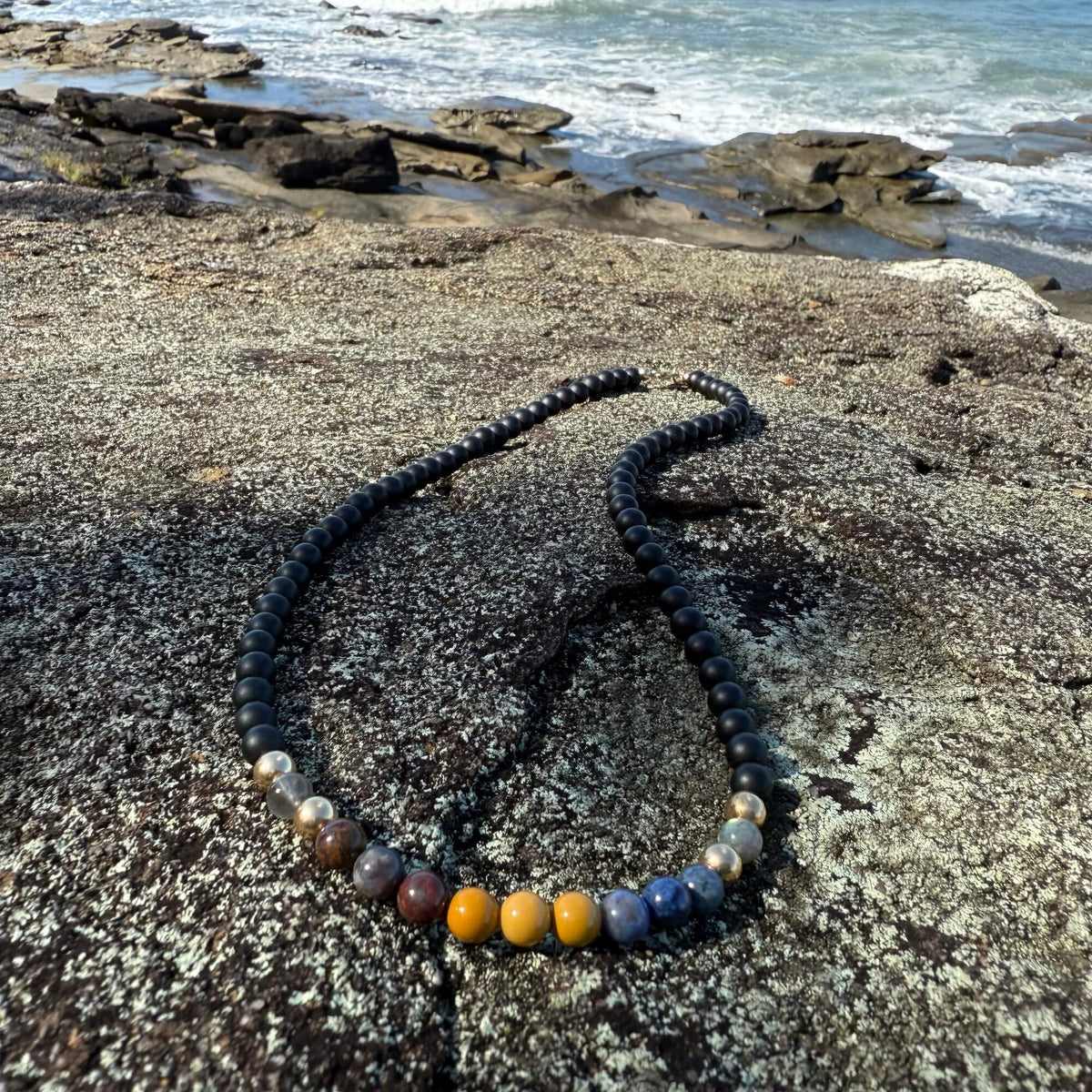Phoenix Rising five-stone necklace on rock with waves breaking behind