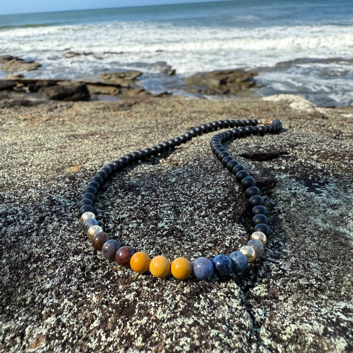 Phoenix Rising necklace laid on rock by the ocean, five-stone section at the front