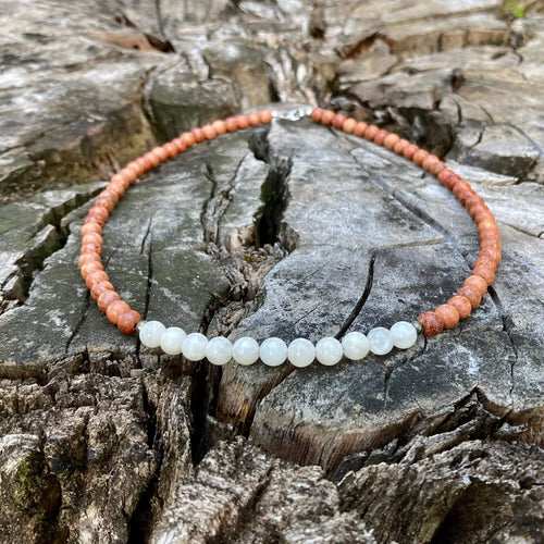 Balance men's necklace: white moonstone with warm natural wood beads, laid on a weathered stump