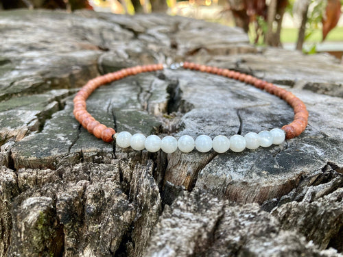 Balance necklace's moonstone section across a cracked tree stump