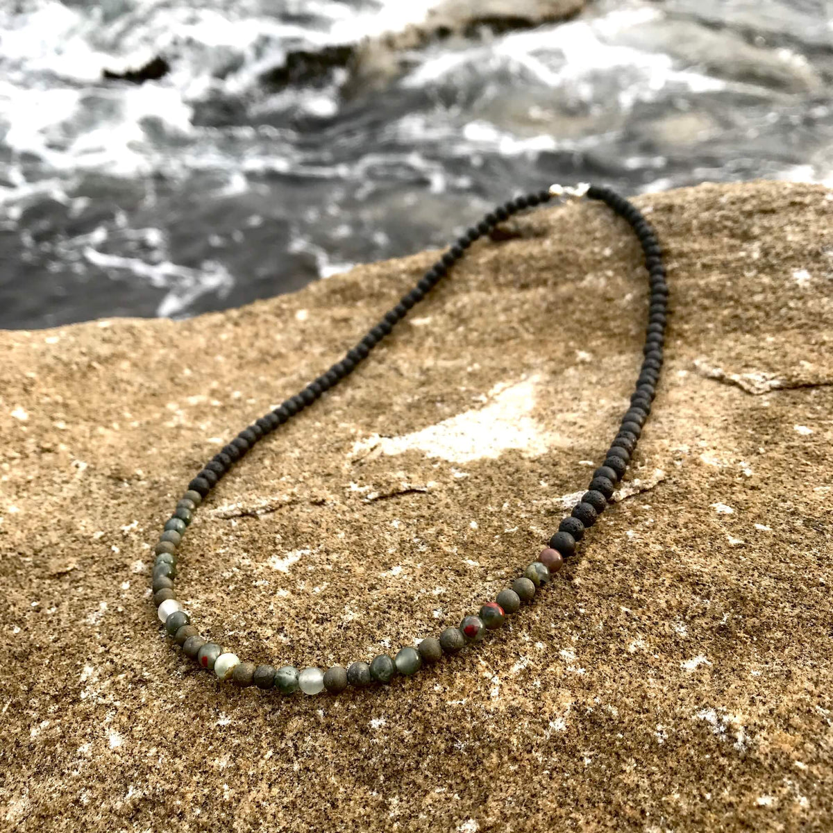 Conviction necklace on coastal rock with water behind