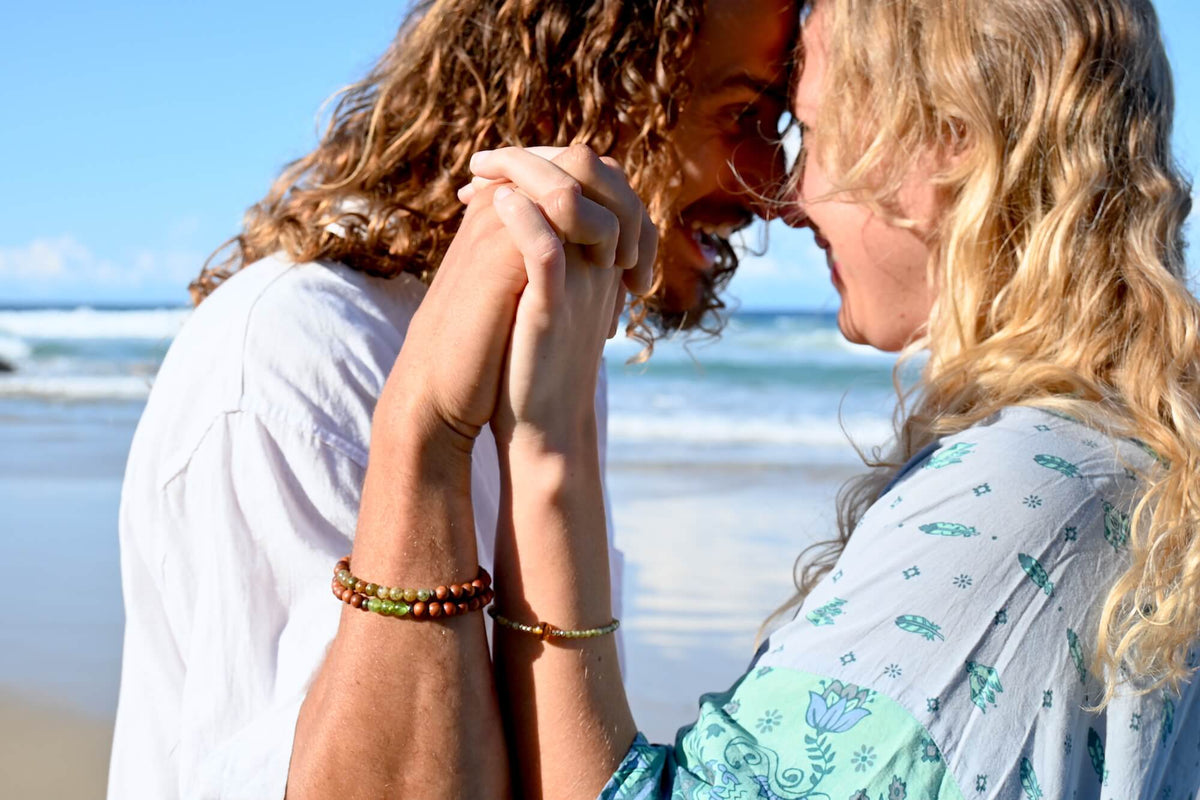 Couple forehead to forehead at the beach, hands clasped, Growth bracelet on his wrist