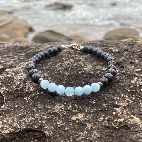 Courage men's bracelet: pale blue aquamarine with matte black lava stone beads, on rock by the sea