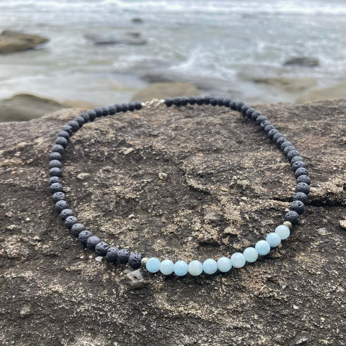 Courage necklace on coastal rock with waves behind