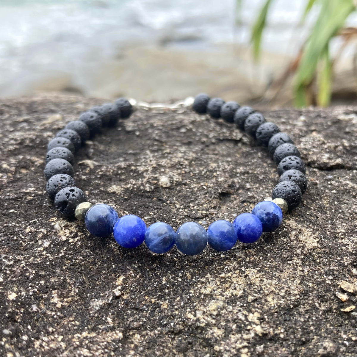 Focus men's bracelet: blue sodalite with matte black lava stone beads, on rock by the sea