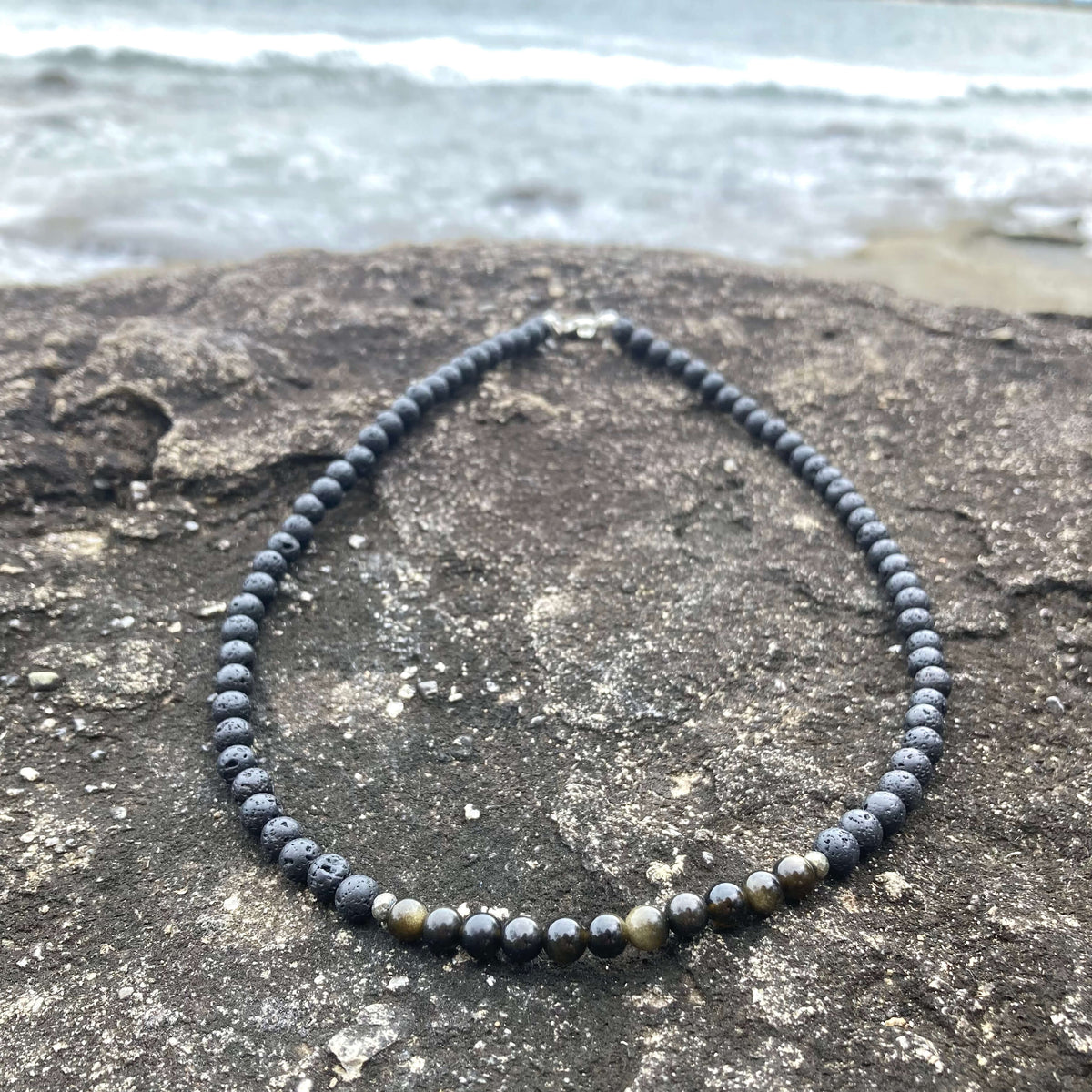 Golden obsidian beads on the Facing Fears necklace, on dark rock
