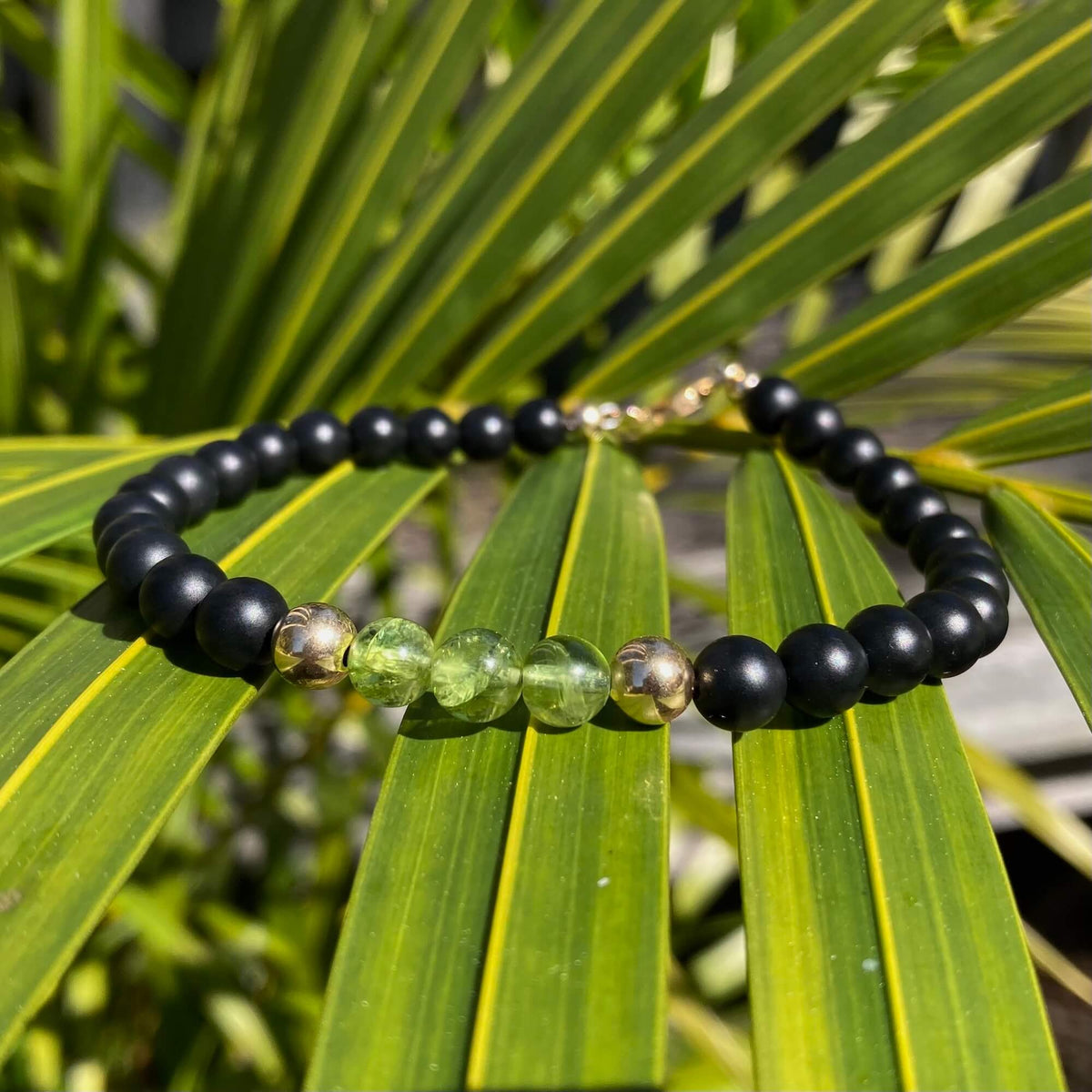 Green peridot beads between black onyx on The Liberator bracelet, on a palm leaf