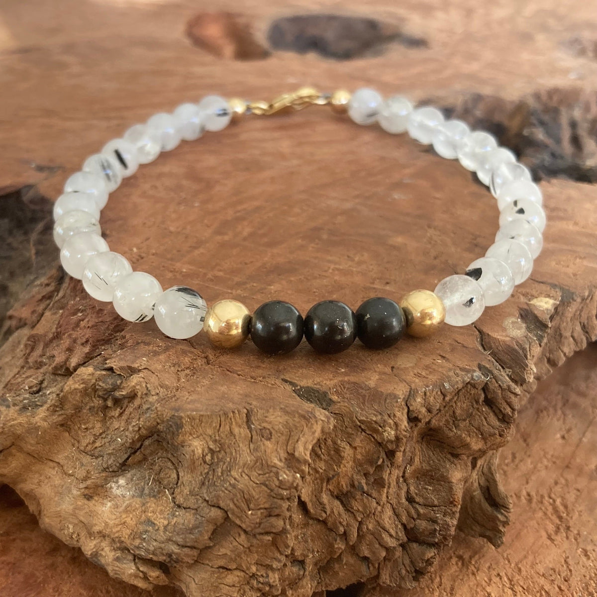 The Integrator men's bracelet: clear tourmalinated quartz with black shungite and 14k gold-fill beads, on wood