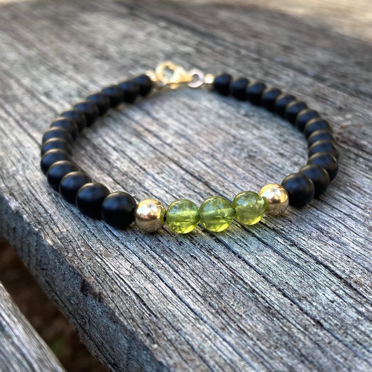 The Liberator men's bracelet: matte black onyx with green peridot and 14k gold-fill beads, on weathered timber
