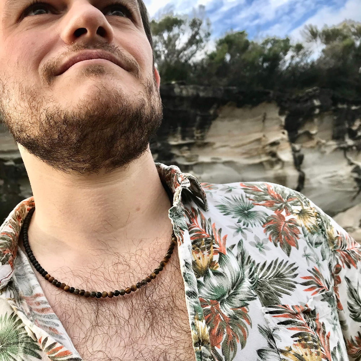 Man by a cliff wearing the Fortitude tiger's eye necklace