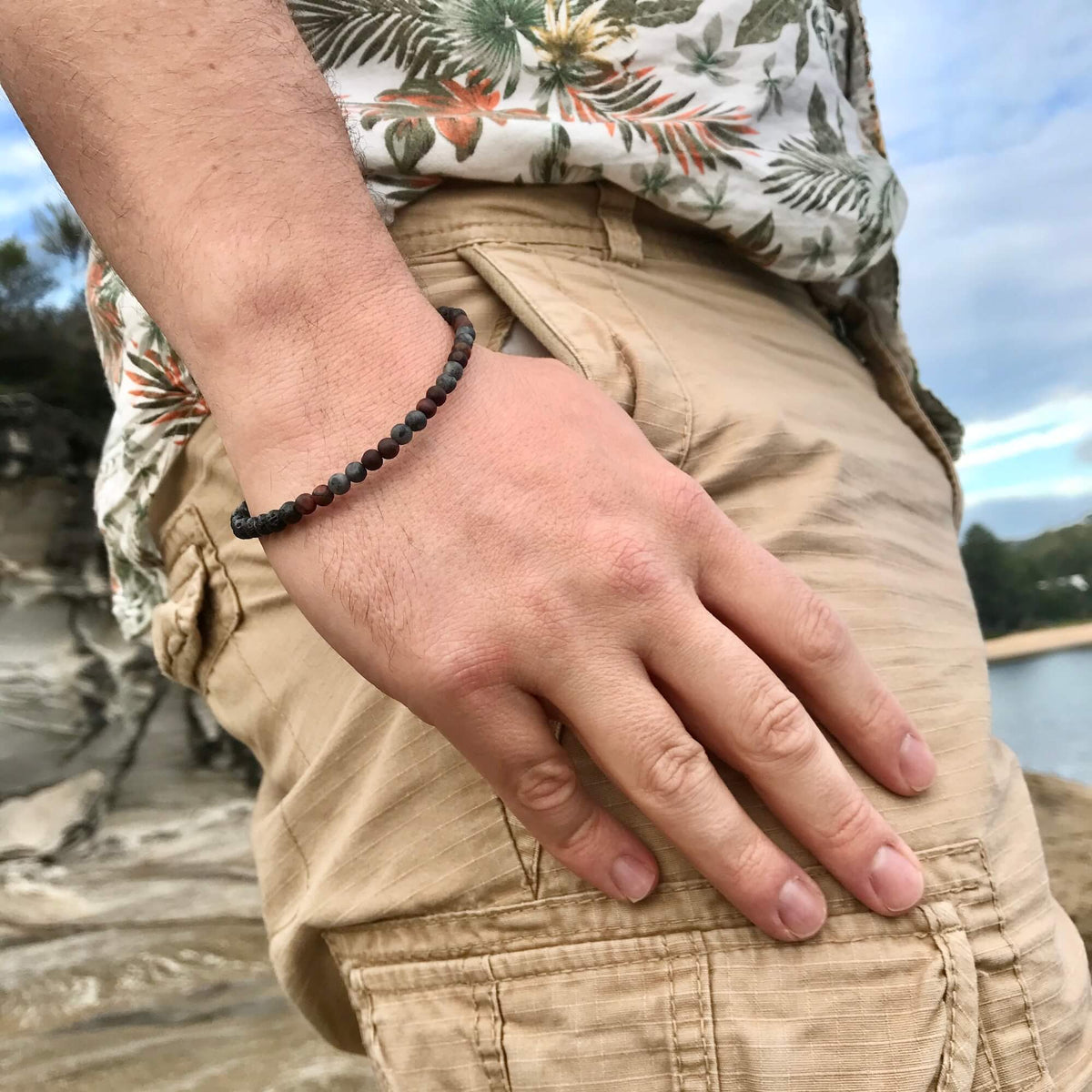Man in a floral shirt and shorts wearing the Drive bracelet by the water