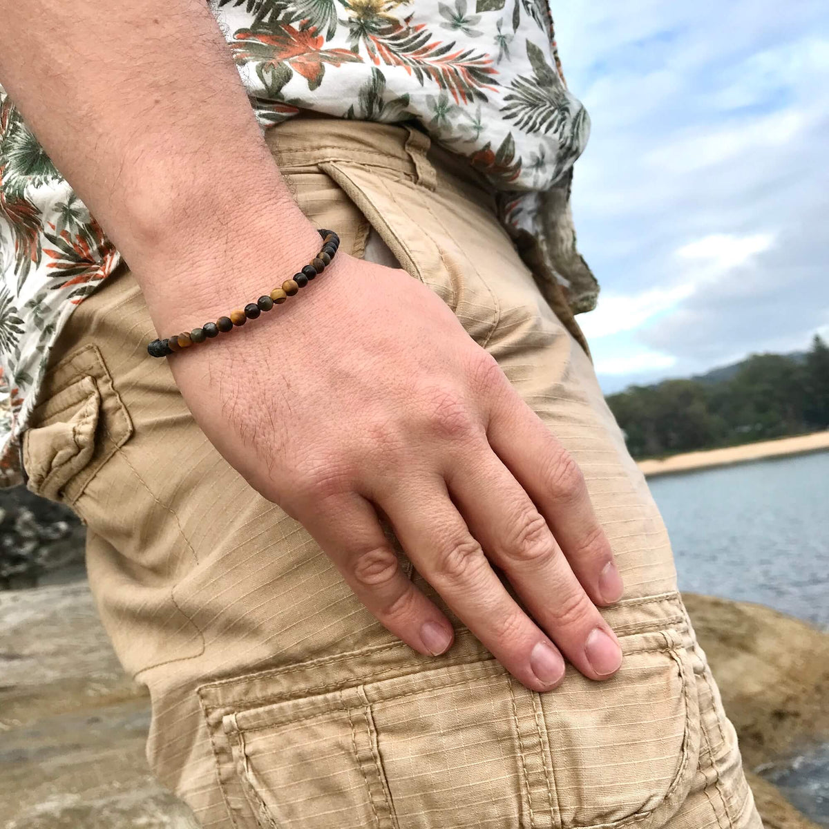 Man in a floral shirt and shorts wearing the Fortitude bracelet by the water