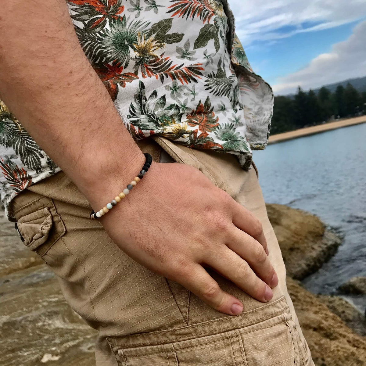 Man in a floral shirt and shorts wearing the Vitality bracelet by the water