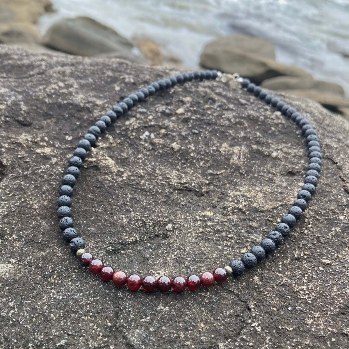 Prosperity necklace on rock with beach stones behind