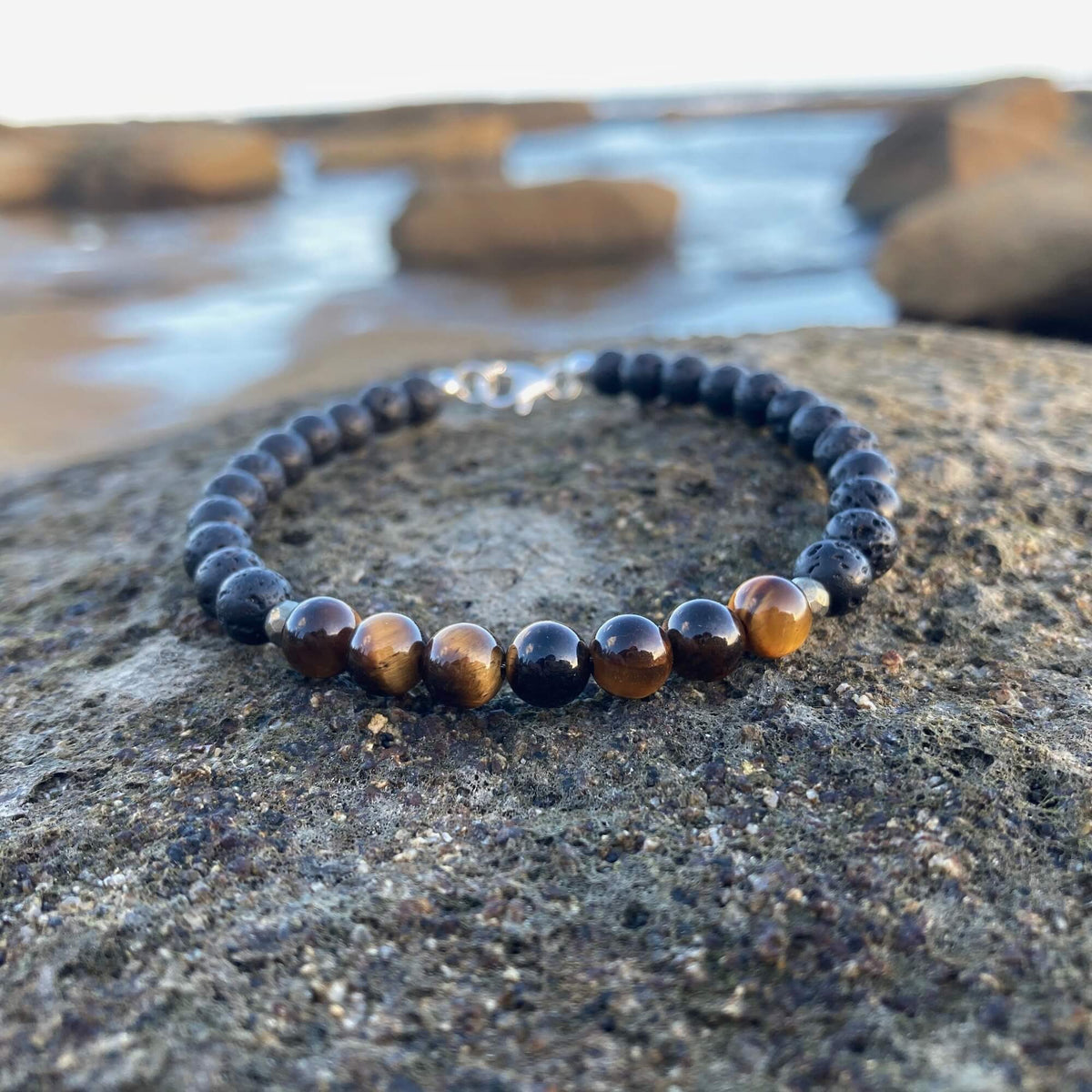 Protection men's bracelet: golden tiger's eye with matte black lava stone beads, on rock by the sea