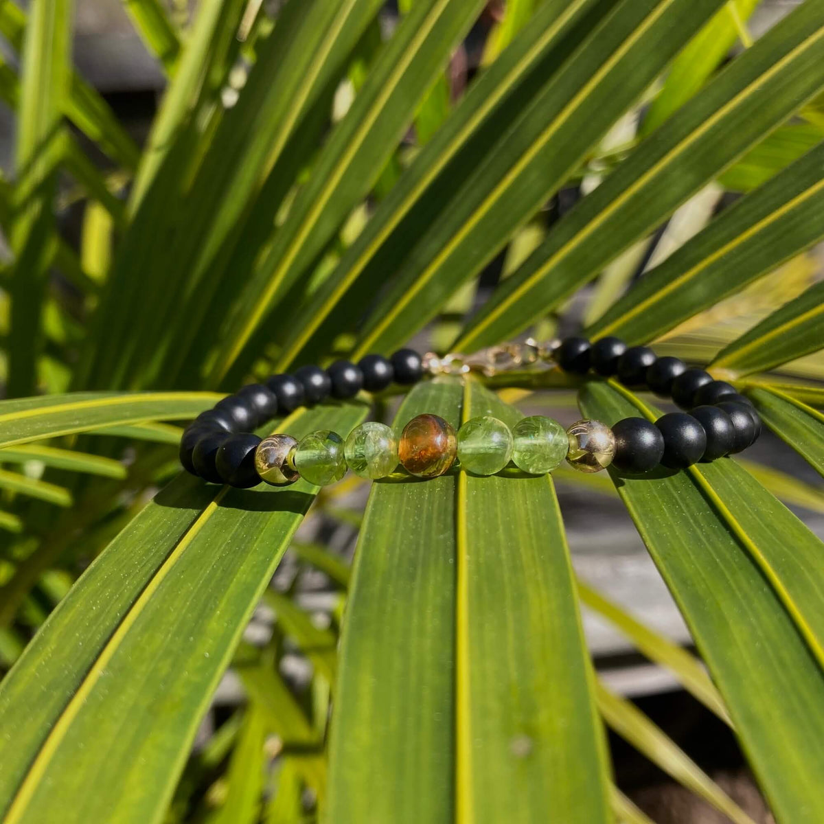 The Renewer bracelet's amber and peridot beads on a palm frond