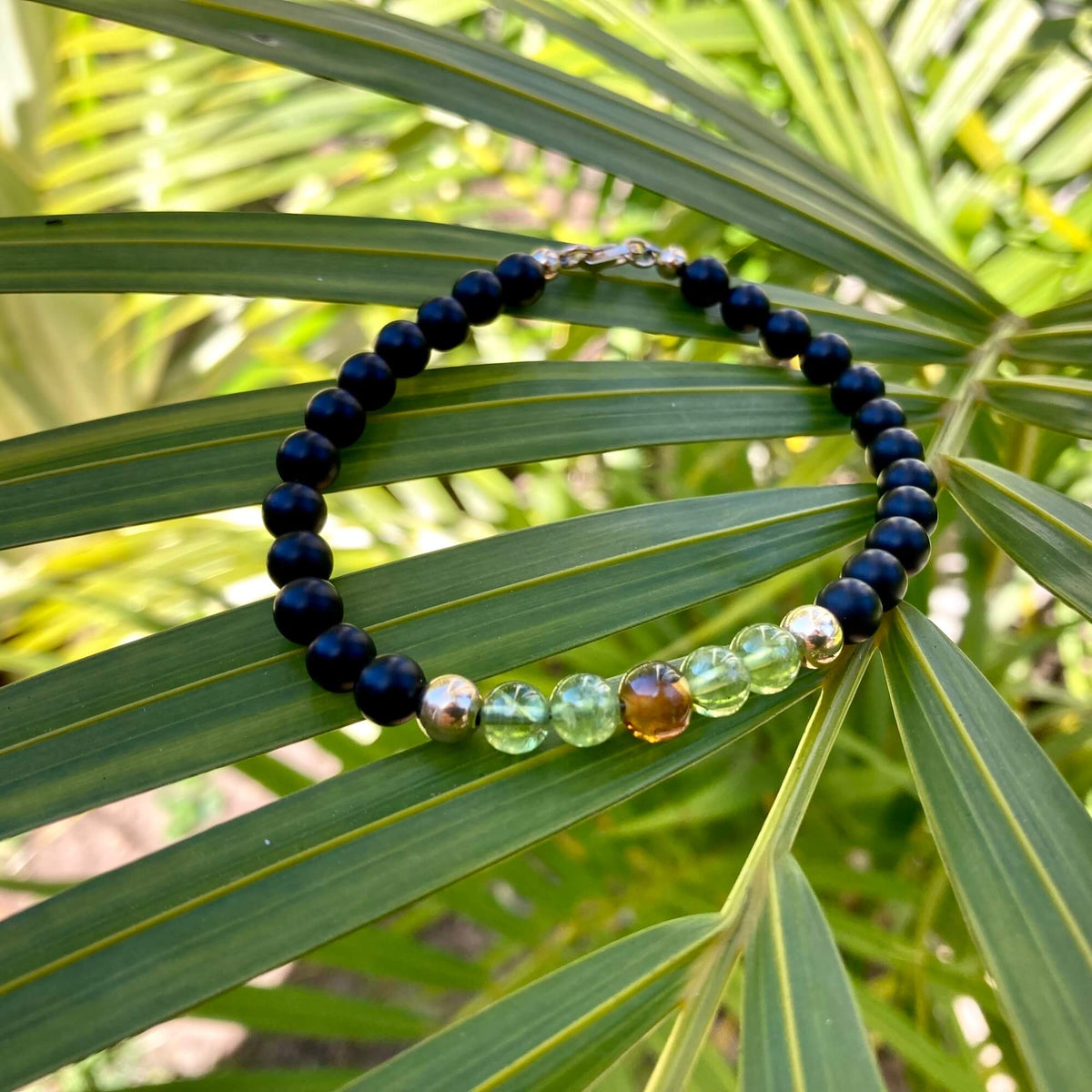 The Renewer bracelet in a circle on palm fronds