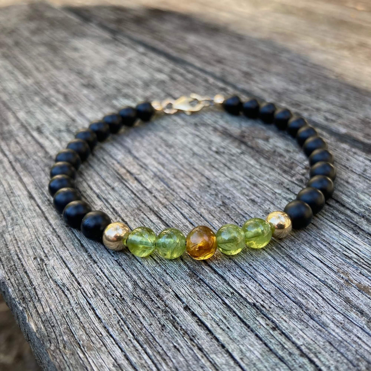 The Renewer men's bracelet: black onyx, green peridot and a Mexican amber centre bead, on weathered timber