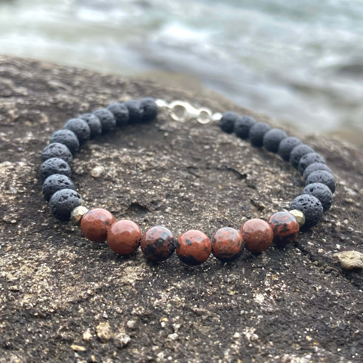 Self-Acceptance men's bracelet: red obsidian with matte black lava stone beads, on rock by the sea