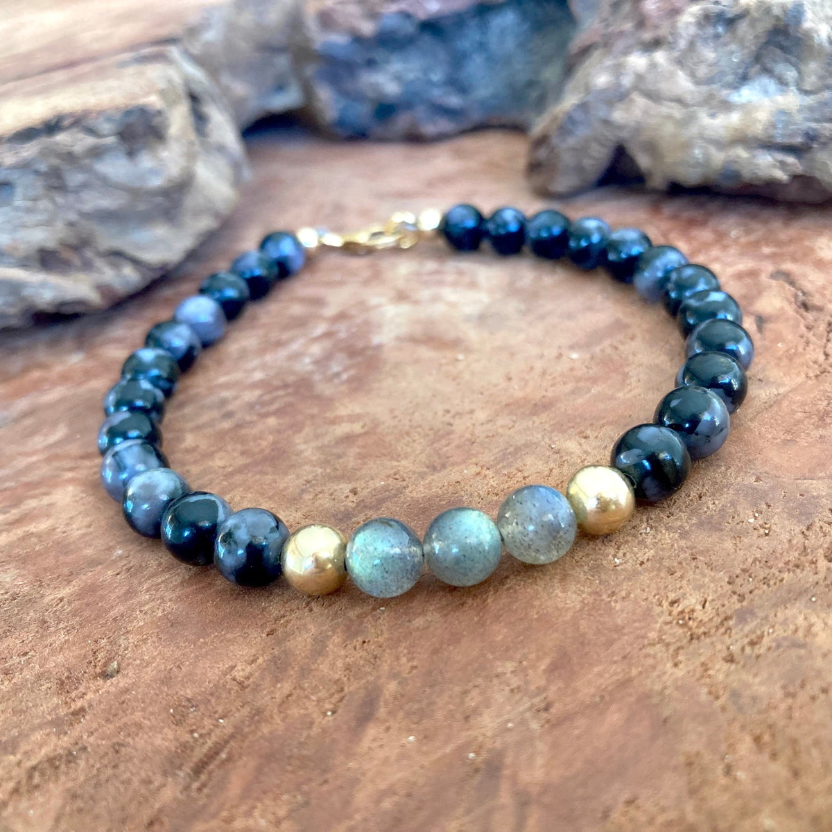 The Shadow Walker men's bracelet: dark merlinite with grey-green labradorite and 14k gold-fill beads, on wood