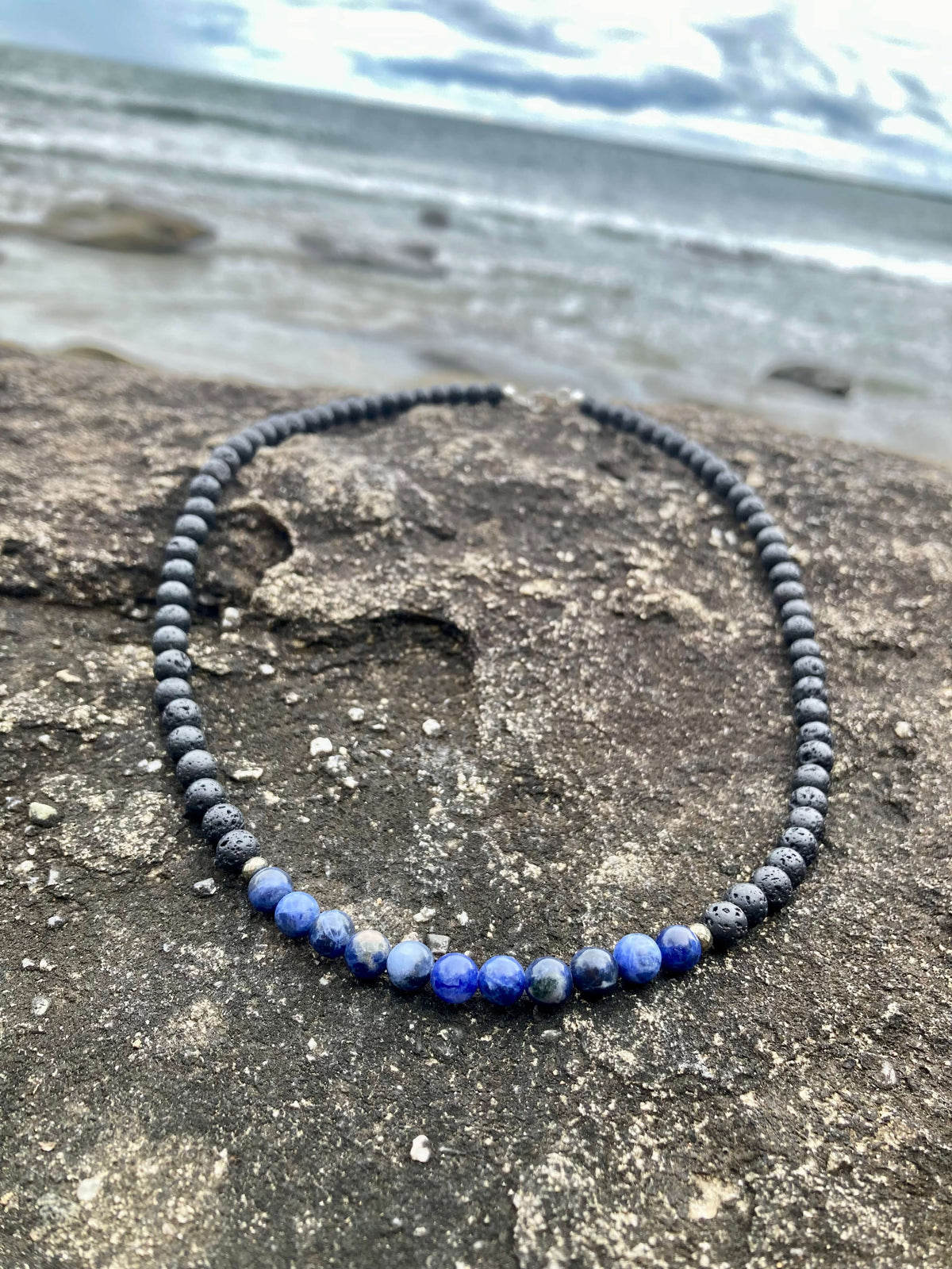 Sodalite section of the Focus necklace on dark rock with waves behind