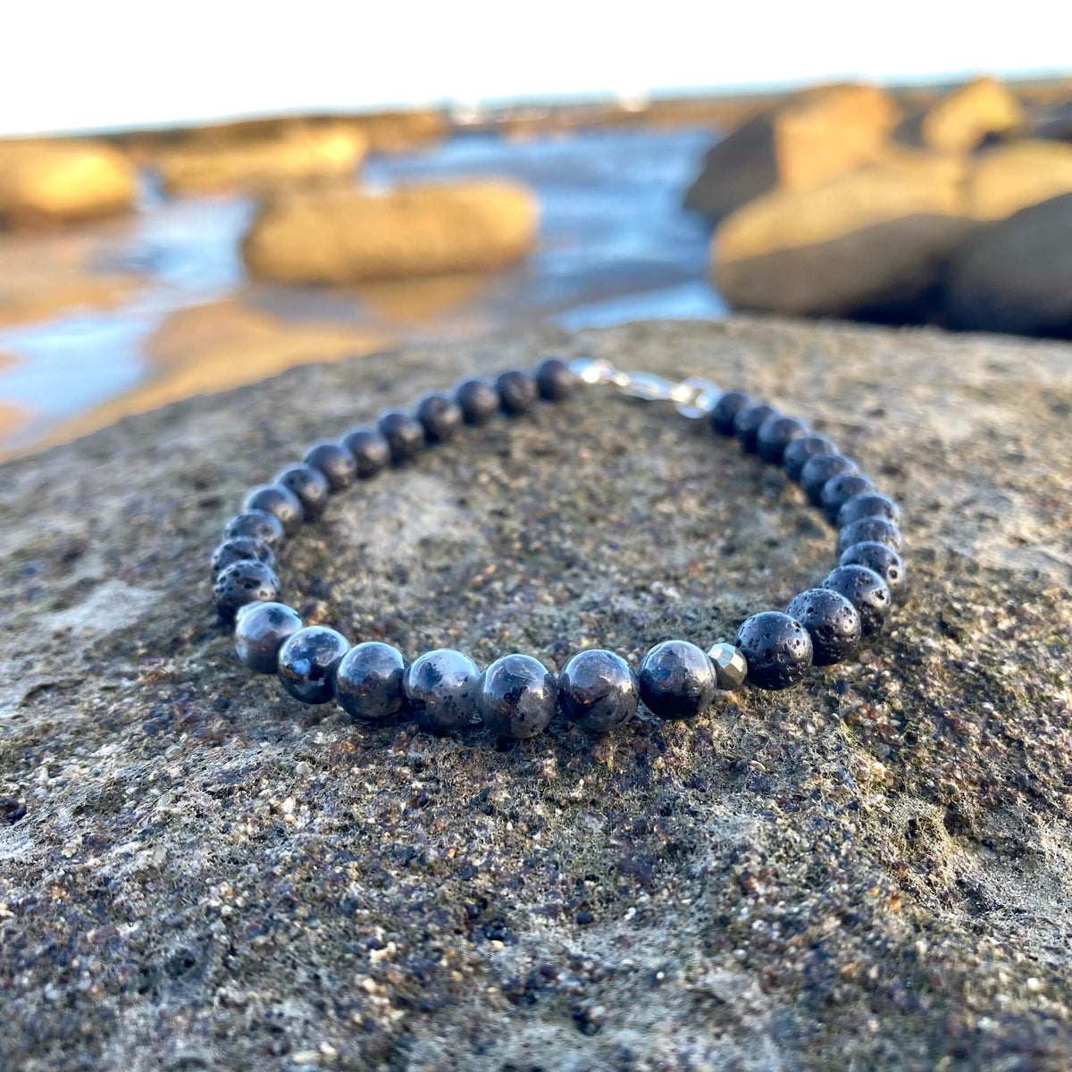 Transformation larvikite bracelet on dark rock with rock pools behind